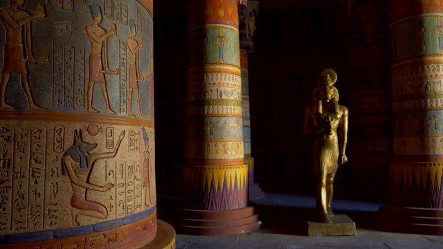 Interior of an Egyptian temple. Colorful columns covered with Ancient Egyptian characters and pictures of ancient people's life. Bronze colored statue of ram headed god Khnum (god of the source of the