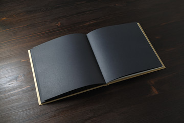 Photo of opened book with blank black pages on wooden background.