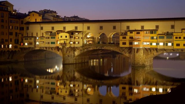 Ponte Vecchio bridge, Florence, Italy. Evening yellow-colored bridge reflecting in Arno River. Panoramic shot, 4K