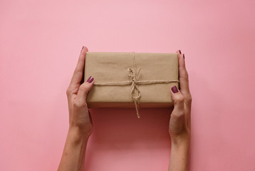 Womans hands holding gift or present box on pink pastel background top view. Flat lay composition for birthday or wedding