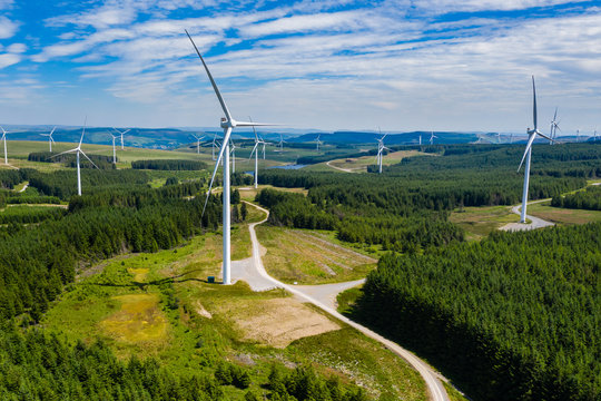 Aerial drone view of turbines at a large onshore windfarm on a green hillside (Pen y Cymoedd, Wales)