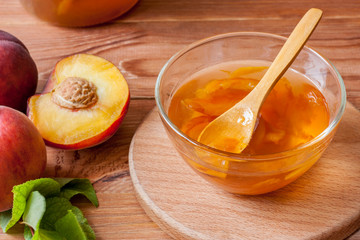 Piala with a spoon in homemade peach jam on a wooden round stand on the table in the morning sun. The concept of homemade conservation. Close up