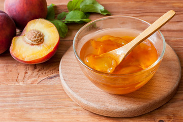 Piala with a spoon in homemade peach jam on a wooden round stand on the table in the morning sun. The concept of homemade conservation. Close up