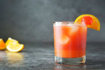 Summer cocktail. Orange juice with mint, syrop, fruit slices and cherry with ice. Dark background.