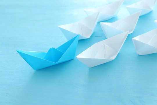 business. Leadership concept image with paper boats on blue wooden background. One leader guiding others.