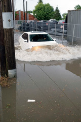 White car driving through flash flooding causing a large wave in front of the car