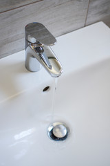 White ceramic sink and nickel-plated brass metallic single-lever tap, faucet  with running water in the bathroom.