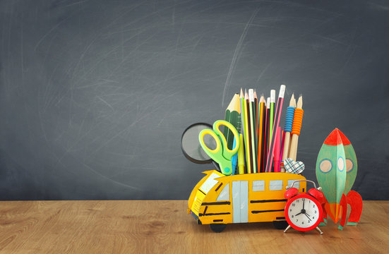 education and back to school concept. pencils stand as bus and cardboard rocket over wooden desk infront of classroom blackboard