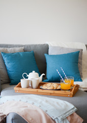 Fototapeta na wymiar Cozy mornings. Breakfast in the living room. Coffee or tea and juice with white blue paper straws, cookies on a wooden tray.