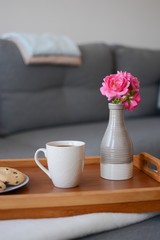 Cozy mornings. Breakfast in the living room. Coffee or tea with cookies on a wooden tray with pink flowers in vase. 