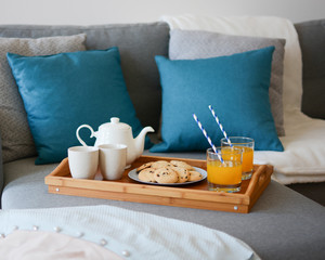 Cozy mornings. Breakfast in the living room. Coffee or tea and juice with white blue paper straws, cookies on a wooden tray.