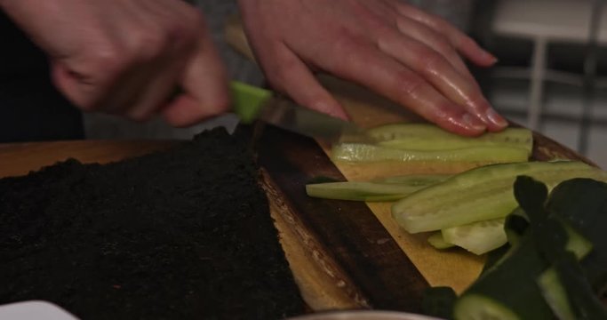 Side view of women hands cutting cucumber on wooden board. Prepering meal.