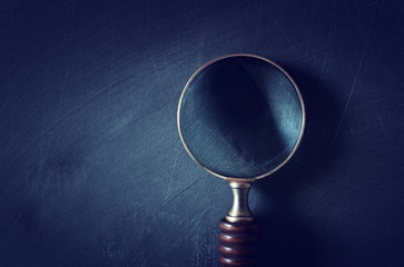 vintage magnifying mlass with wooden handle over chalkboard background. top view, flat lay