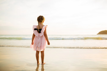 Cute little girl walking on the beach. Sunset time. Kid having fun in holiday vacation with back sun light - Youth, lifestyle, travel and happiness concept