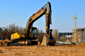 Yellow excavator at a construction site during earthworks and laying of underground pipes and communications in the city