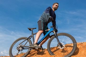 Naklejka premium Cyclist in shorts and jersey on a modern carbon hardtail bike with an air suspension fork rides off-road on the orange-red hills at sunset evening in summer 