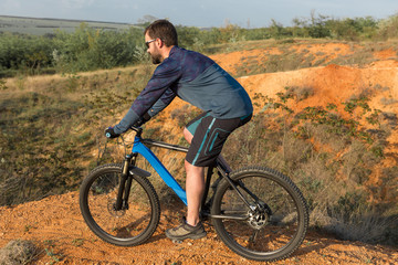 Fototapeta na wymiar Cyclist in shorts and jersey on a modern carbon hardtail bike with an air suspension fork rides off-road on the orange-red hills at sunset evening in summer 