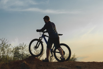Fototapeta na wymiar Cyclist in shorts and jersey on a modern carbon hardtail bike with an air suspension fork rides off-road on the orange-red hills at sunset evening in summer 