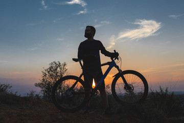 Obraz premium Cyclist in shorts and jersey on a modern carbon hardtail bike with an air suspension fork rides off-road on the orange-red hills at sunset evening in summer 