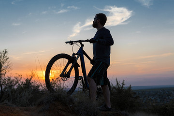 Obraz premium Cyclist in shorts and jersey on a modern carbon hardtail bike with an air suspension fork rides off-road on the orange-red hills at sunset evening in summer 