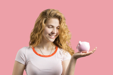Young red-haired curly girl holding piggy bank and rejoices gesturing. The concept of reliability of cash investments and insurance.