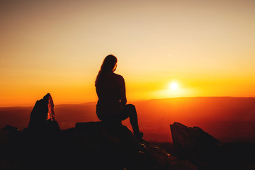 A girl silhouette sitting chilling on the mountain top and watching sunset on a warm summer day. Torfhaus, National Park Harz in Germany