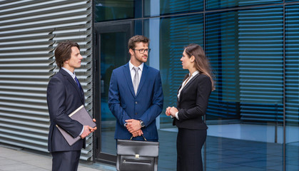 Fototapeta premium Confident businesspersons talking in front of modern office building. Businessmen and businesswoman have business conversation. Banking and financial market concept.