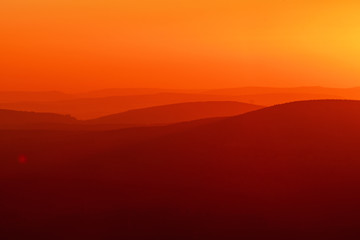 Colorful orange and red tones of a mountain abstract sunset view with dust and glowing light and layer silhouettes. Torfhaus, National Park Harz in Germany