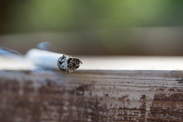 Burning cigarette on wooden surface close up macro shot, conceptual image of human negligence.