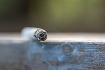 Burning cigarette on wooden surface close up macro shot, conceptual image of human negligence.