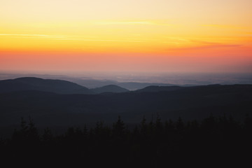 Mountain landscape wide area panorama view from the top down to the valley and endless forest trees. Colorful sunset with summer clear sky.