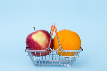red apple fnd orange in grocery cart on blue background