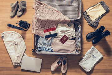 Woman's clothes, laptop, camera, russian passport and flag of Egypt lying on the parquet floor near and in the open suitcase. Travel concept