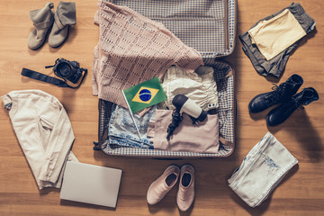 Woman's clothes, laptop, camera and flag of Brazil  lying on the parquet floor near and in the open suitcase. Travel concept