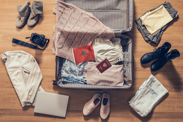 Woman's clothes, laptop, camera, russian passport and flag of Morocco lying on the parquet floor near and in the open suitcase. Travel concept