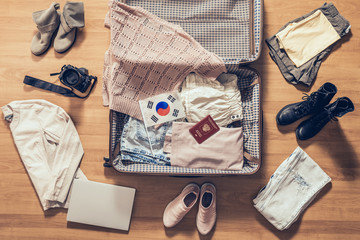 Woman's clothes, laptop, camera, russian passport and flag of South Korea lying on the parquet floor near and in the open suitcase. Travel concept