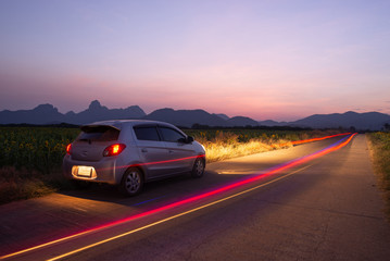Plakat Travel car is parking at the road country side with landscape view beautiful sunset and light trails.