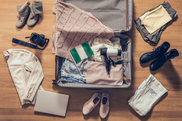 Woman's clothes, laptop, camera and flag of Nigeria lying on the parquet floor near and in the open suitcase. Travel concept