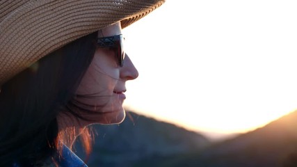 Close-up smiling beautiful face of travel woman in hat and sunglasses at mountain sunset background