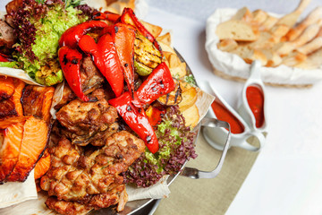 Mixed grill meat, fried vegetables and grilled salmon fish fillets decoration in warm dish. Assorted delicious grilled kebab served with herbs on platter. Restaurant menu plate