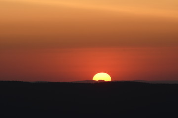 Giant sun with mountain sunset and silhouettes and warm orange color tones. Torfhaus, National Park...