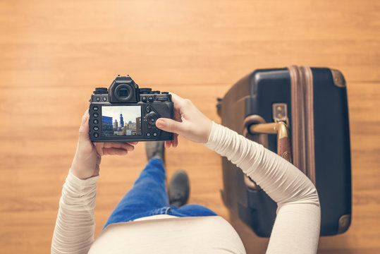 Top view on a girl looking a photos Chicago city on her camera standing with suitcase in the airport. The girl returns home after trip to America.