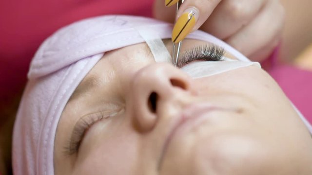 Eyelash Extension in modern Beauty salon. Woman Eye with long Eyelashes. Professional Beautician with tweezers is making eyelash extension to client at Cosmetic Procedure.