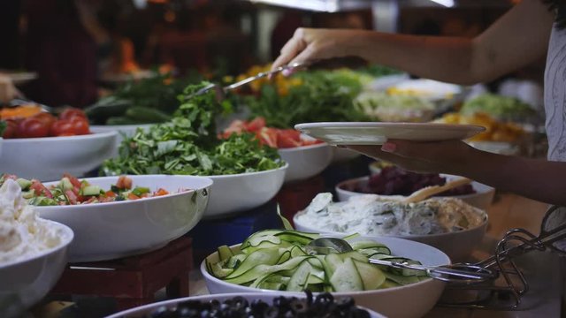 A woman puts on a plate of greens. Breakfast buffet in the restaurant, close-up.