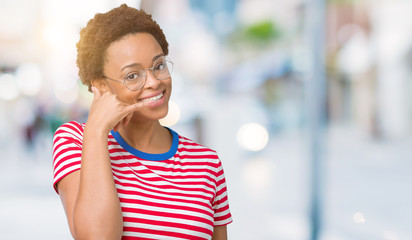 Beautiful young african american woman wearing glasses over isolated background smiling doing phone gesture with hand and fingers like talking on the telephone. Communicating concepts.