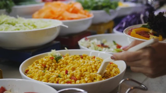 Woman puts canned corn in a bowl from the buffet in the hotel restaurant, close-up.