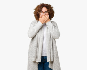 Beautiful middle ager senior woman wearing jacket and glasses over isolated background shocked covering mouth with hands for mistake. Secret concept.