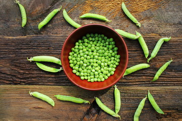 Green peas in bowl on wooden table background. Top view