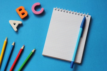 Fototapeta na wymiar ABC-the first letters of the English alphabet on a blue background. Notebook and pen. Empty space for text. Learn foreign languages.