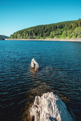 Rocks in the water at a mountain lake with perfect weather. Okertalsperre. Torfhaus in National Park Harz in Germany